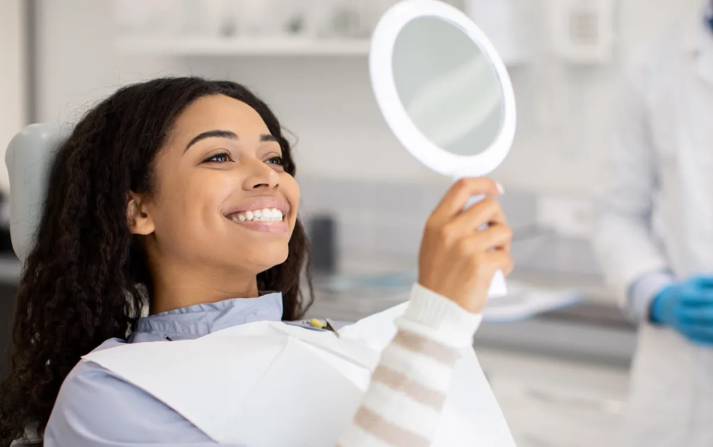 Smiling patient holding a mirror in a dental office, showcasing satisfaction with cosmetic dentistry results at Dr. Thu Nguyen's practice in Anaheim.