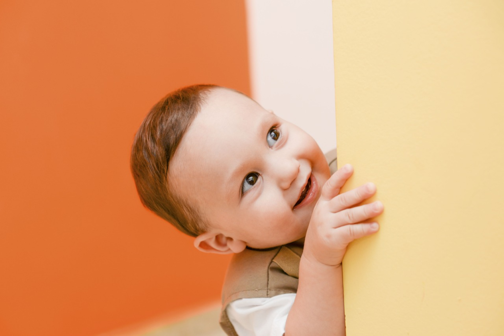 Smiling child peeking around a yellow wall in a colorful pediatric dental office, illustrating a welcoming environment for children's dental care.