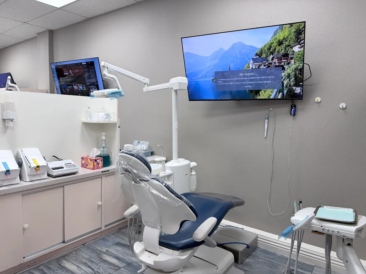 Dental treatment room at Anaheim Implants & Dental Group featuring a dental chair, medical equipment, and a large screen displaying a scenic landscape.