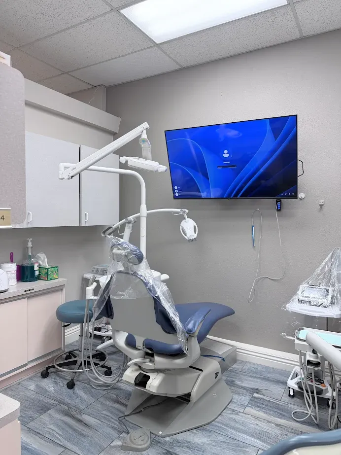 Modern dental exam room with blue chair, equipment, and wall-mounted TV